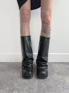Black knee-high boots worn with a plain background