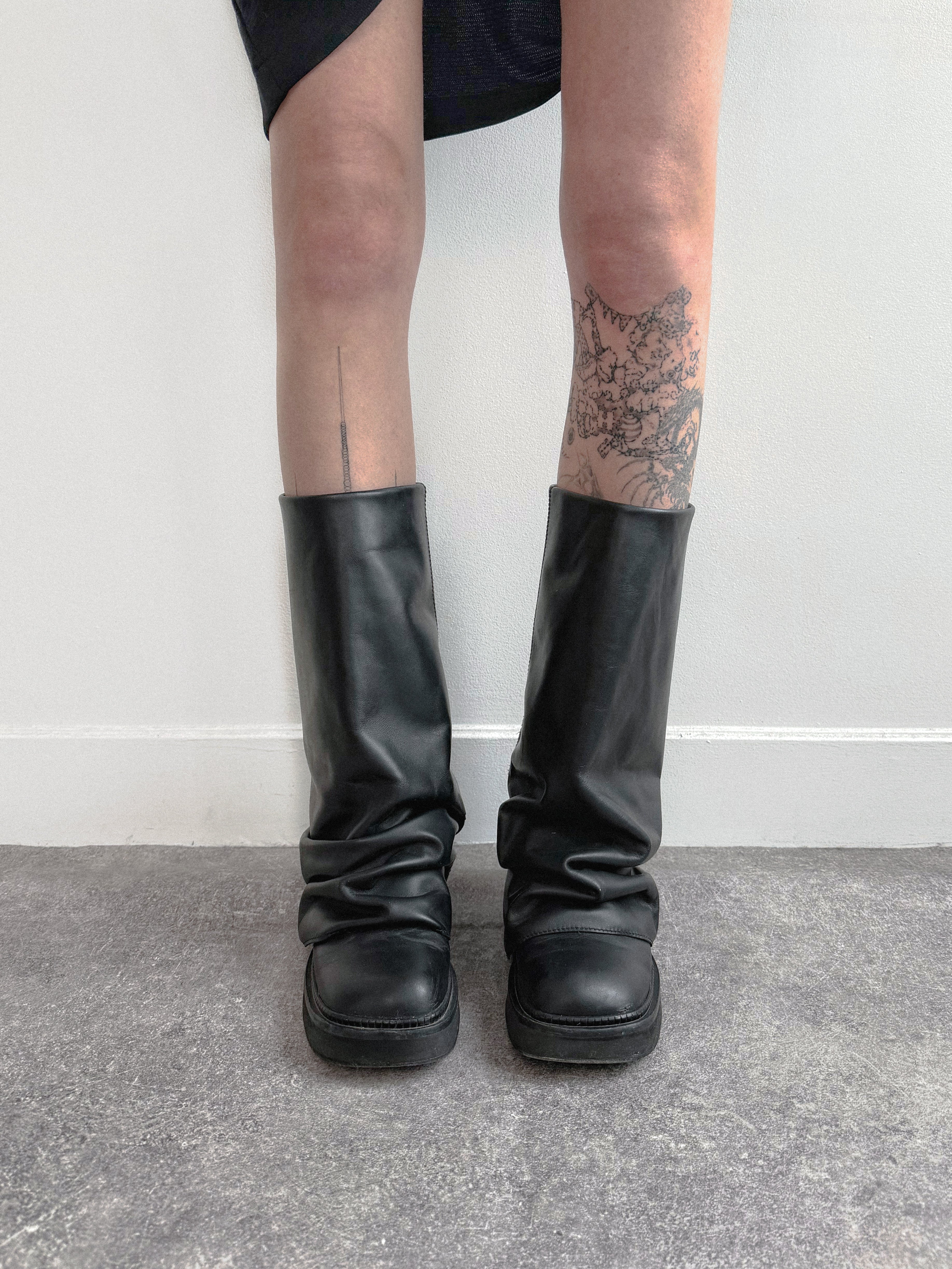 Black knee-high boots worn with a plain background