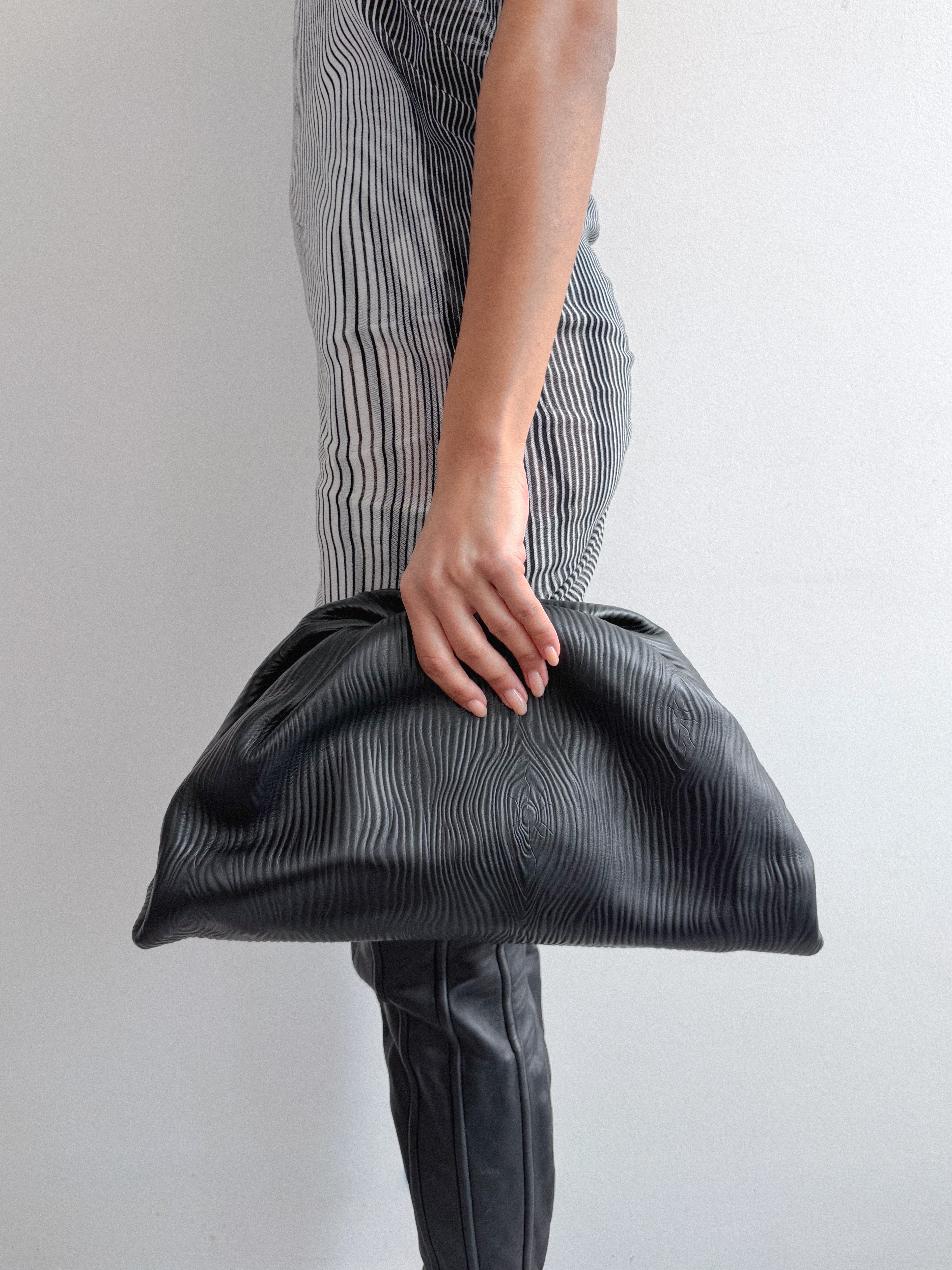 Person holding a textured black clutch bag against a plain background