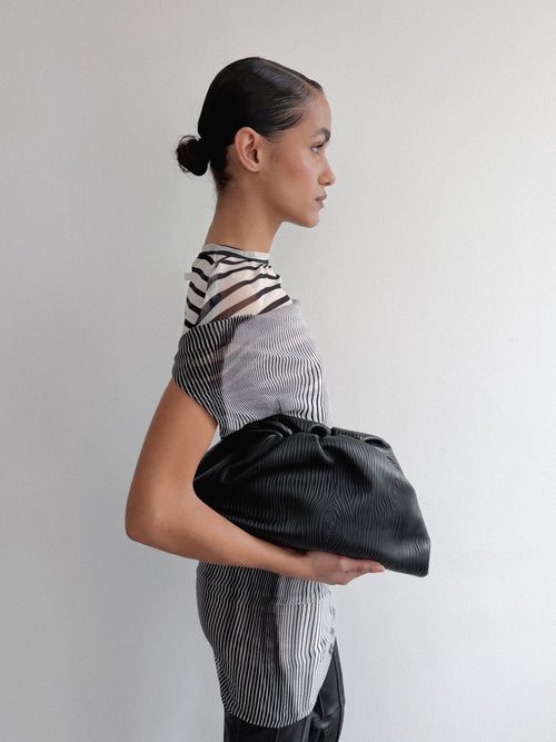 Woman holding a black clutch against a plain background
