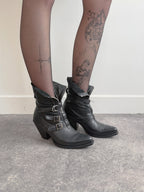 Black leather boots with buckles worn by a person on a neutral background