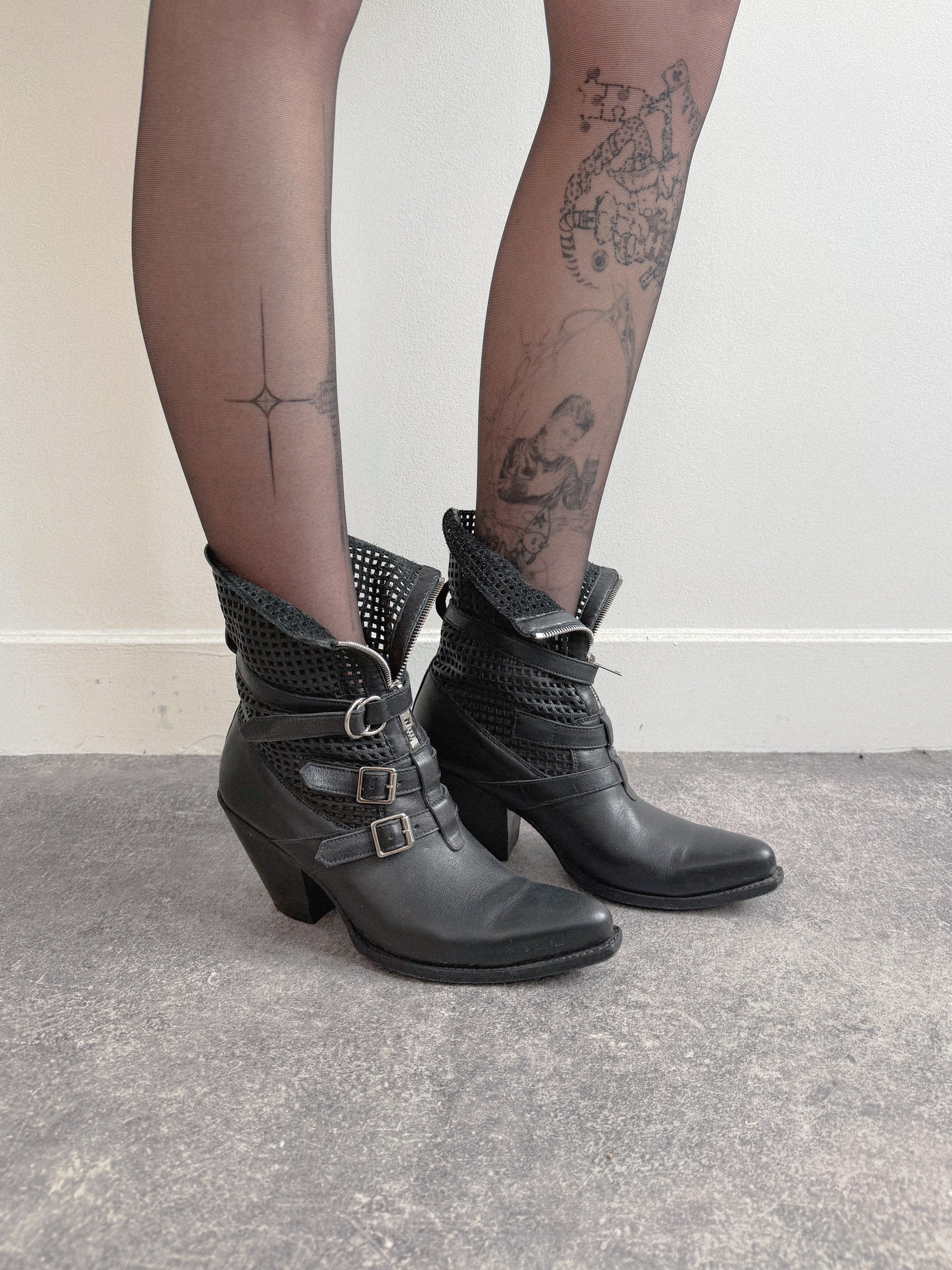 Black leather boots with buckles worn by a person on a neutral background