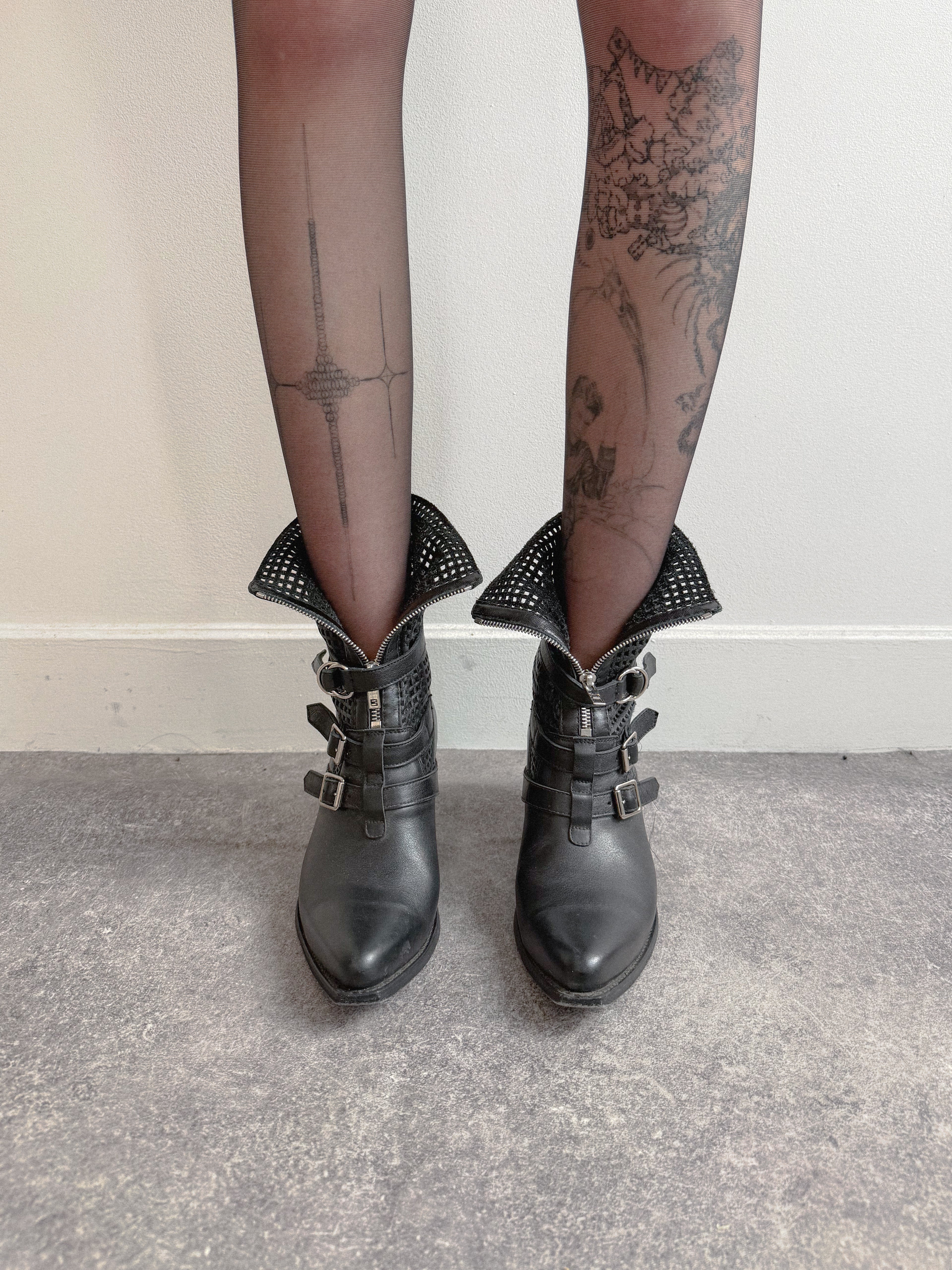 Black leather boots worn with sheer black tights against a neutral background