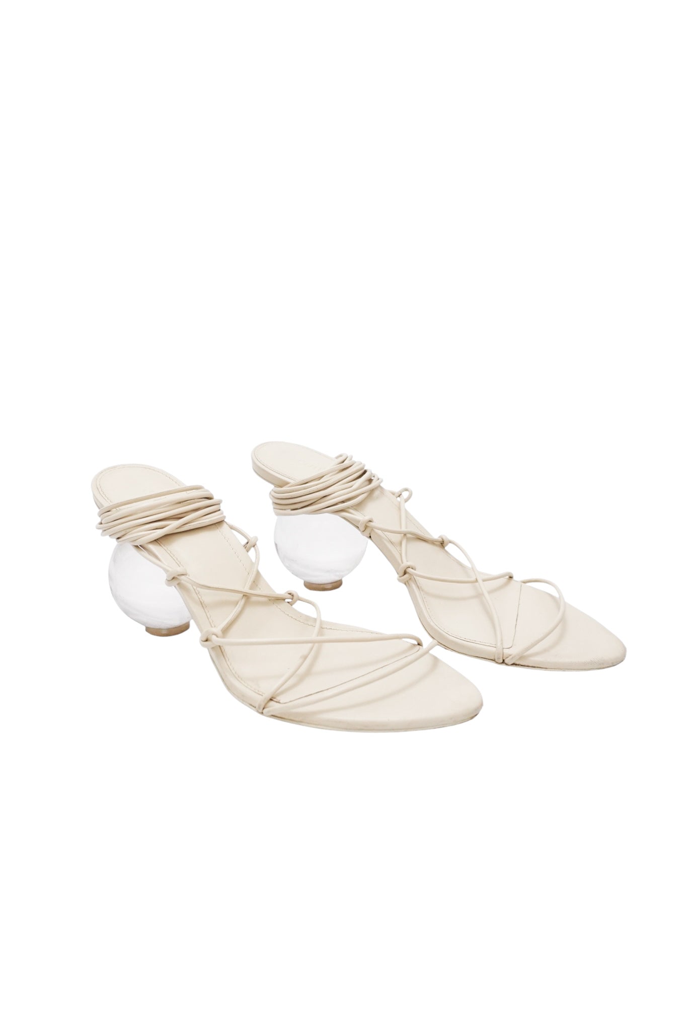 Pair of beige strappy sandals with white spherical elements on a white background