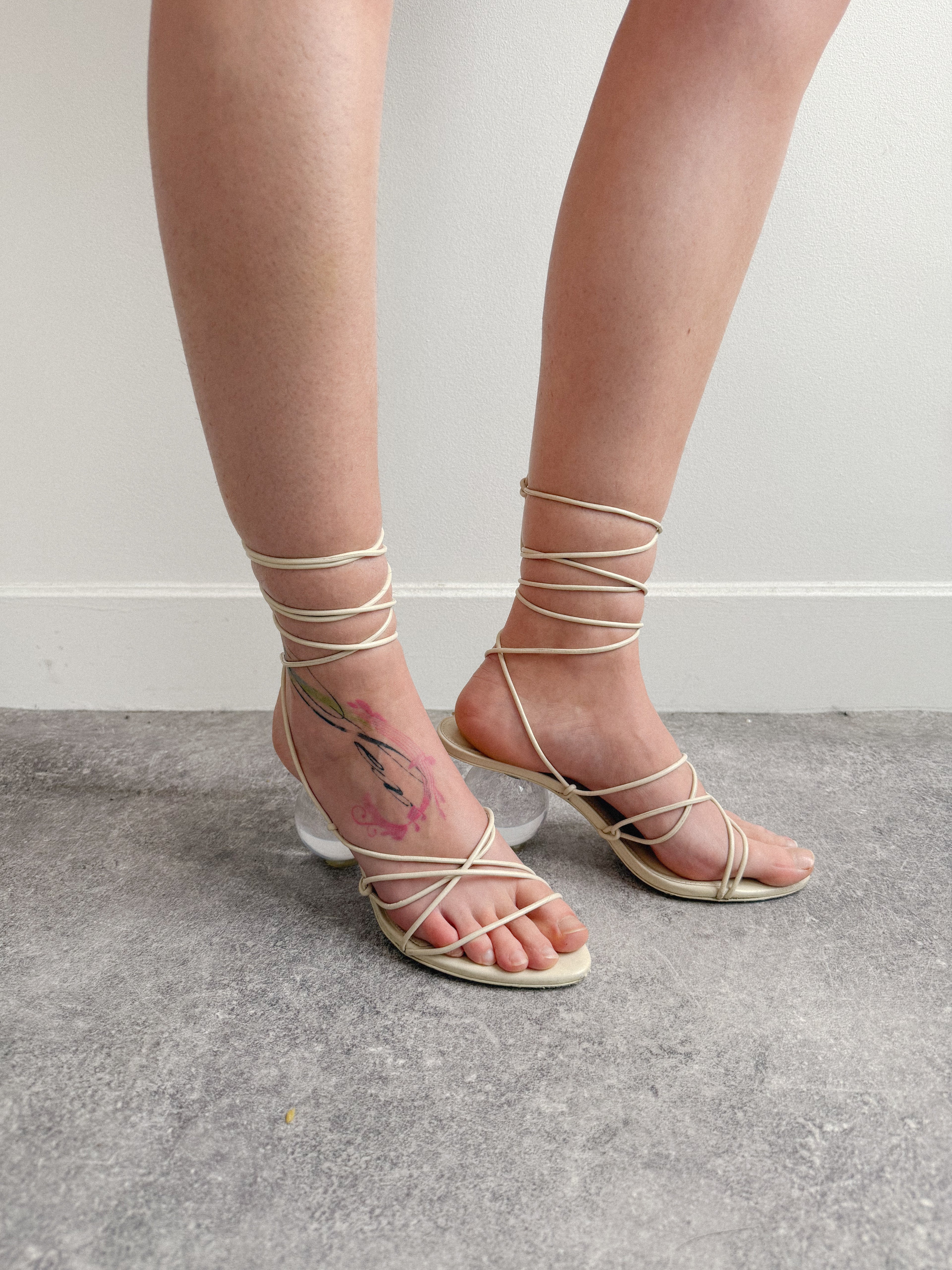 Strappy sandals worn with minimal clothing on a neutral background