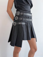 Black skirt with silver buckles worn by a person on a light gray background