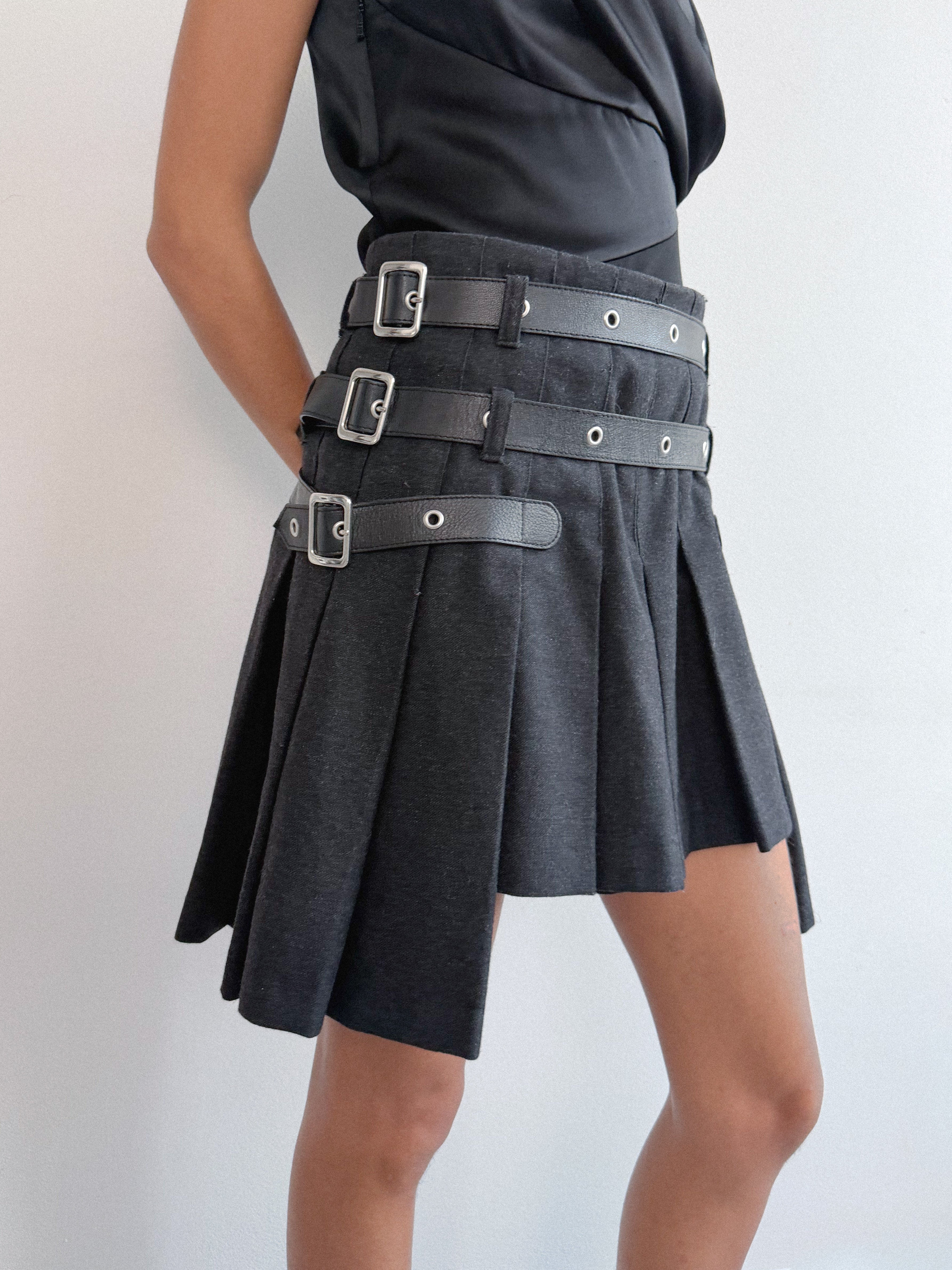Black skirt with silver buckles worn by a person on a light gray background