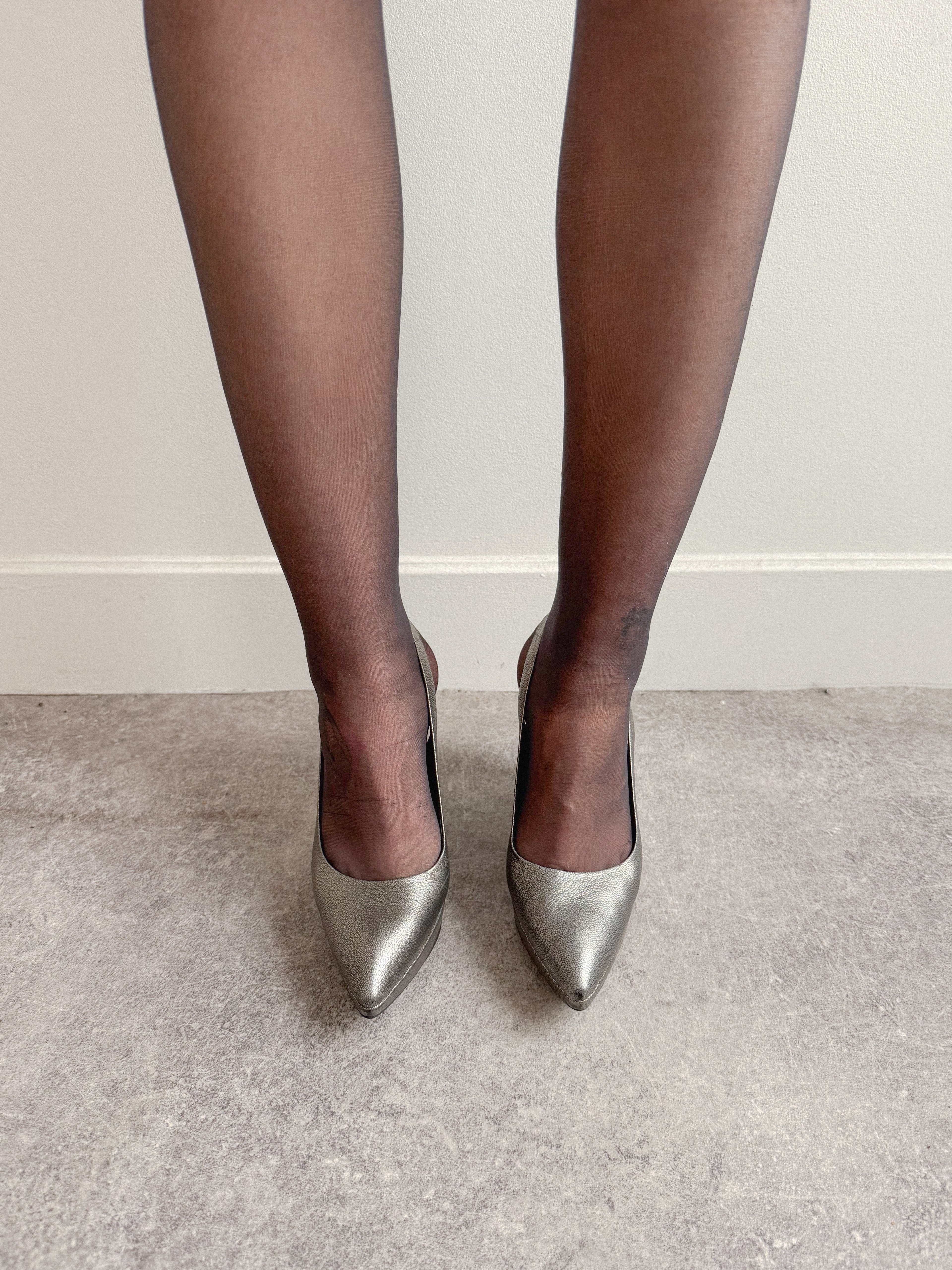 Silver high-heeled shoes worn with black tights on a neutral background