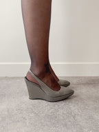 Gray wedge sandals worn with brown tights on a neutral background