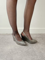 Person wearing silver wedge heels and black tights on a neutral background