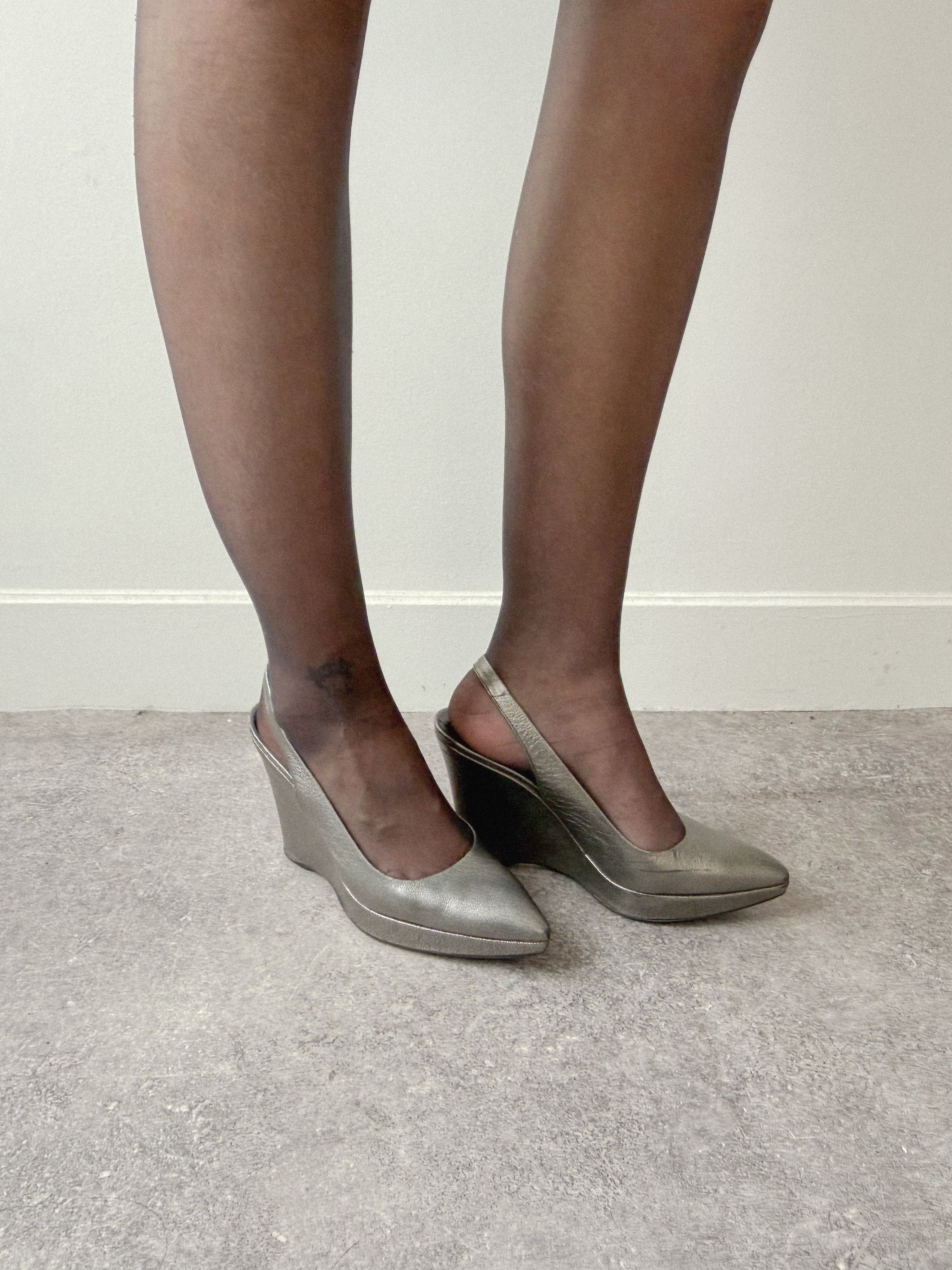 Person wearing silver wedge heels and black tights on a neutral background