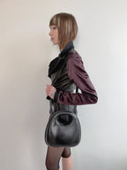Person wearing a dark outfit with a large black handbag against a plain background