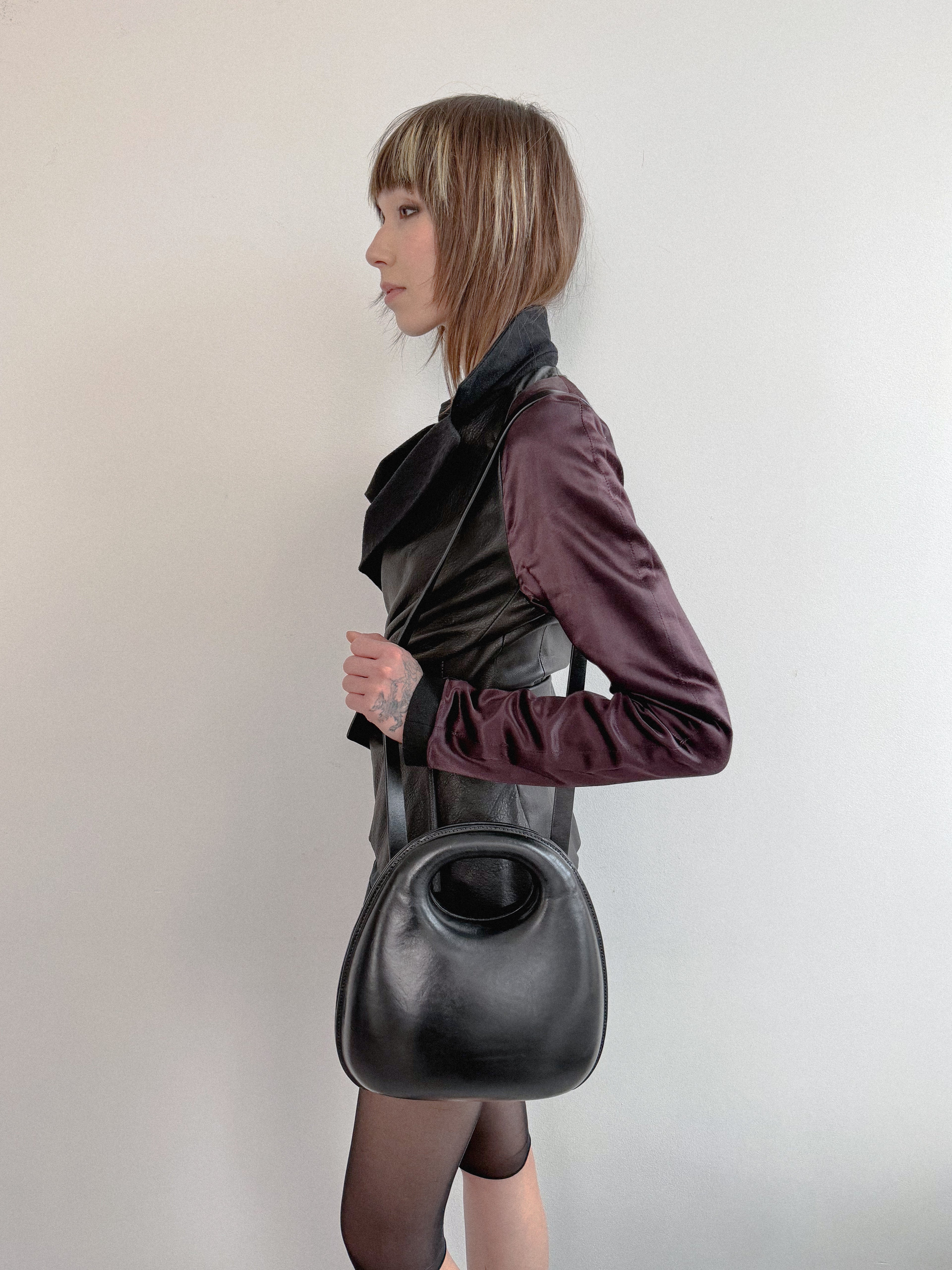 Person wearing a dark outfit with a large black handbag against a plain background