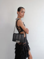 Woman holding a black handbag against a plain background