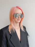 Person with pink hair wearing futuristic sunglasses against a plain background