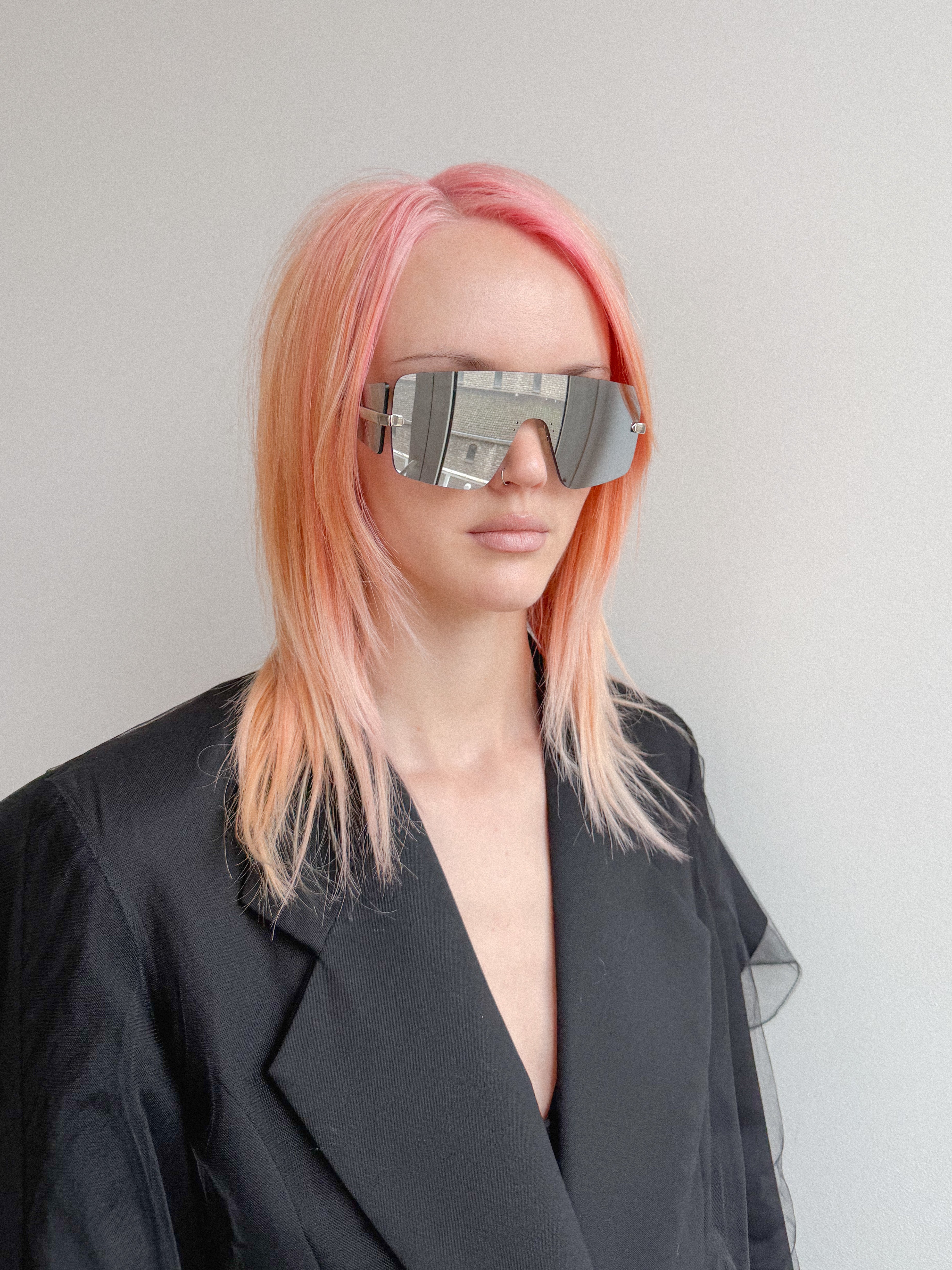 Person with pink hair wearing futuristic sunglasses against a plain background