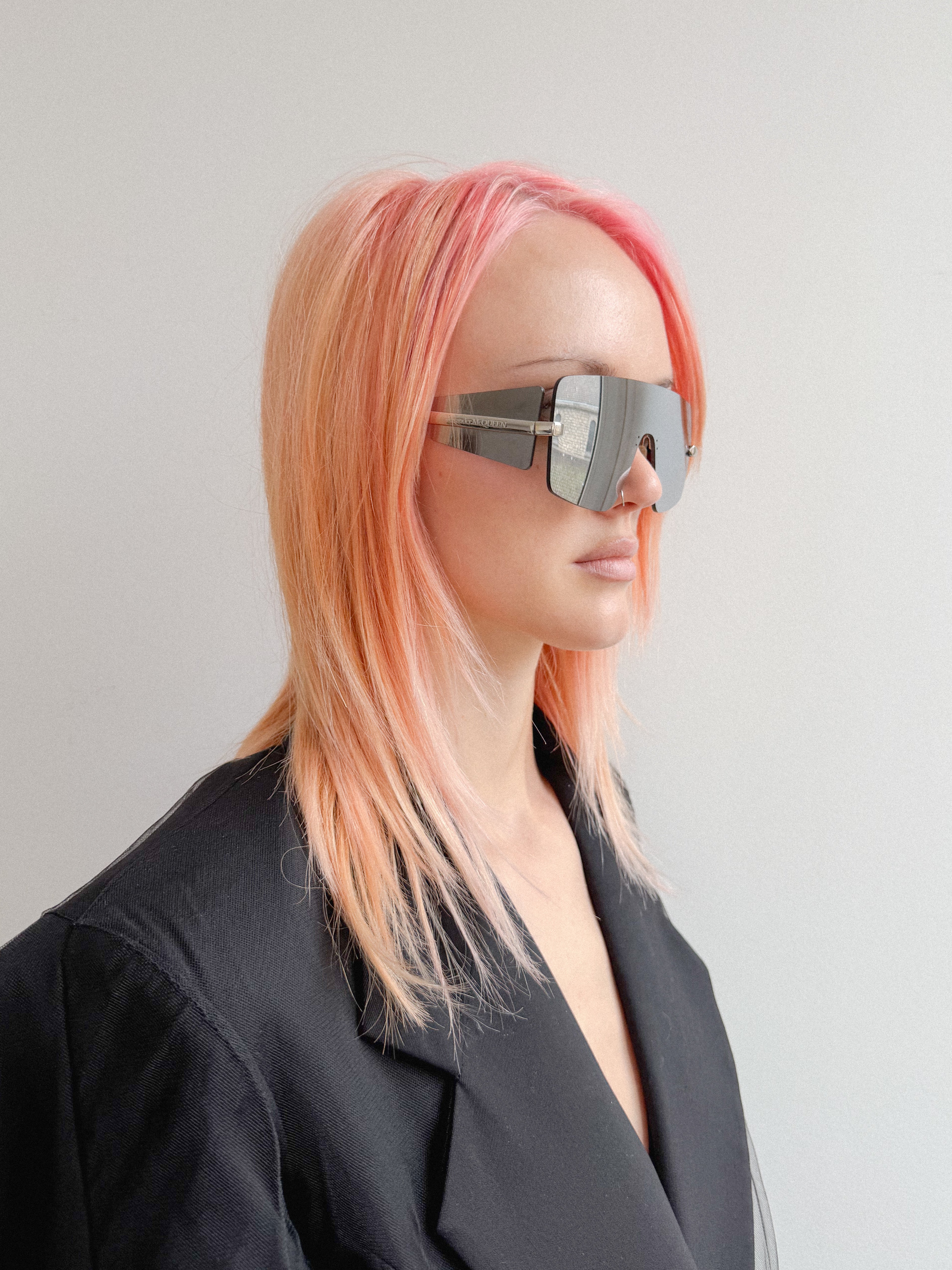 Person with pink hair wearing futuristic sunglasses against a plain background
