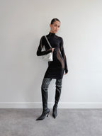 Person wearing a black outfit with geometric patterns and high-heeled boots against a plain background