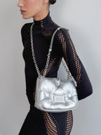 Person wearing a black outfit with a silver handbag on a plain background