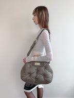 Woman carrying a large gray bag on her shoulder against a plain background