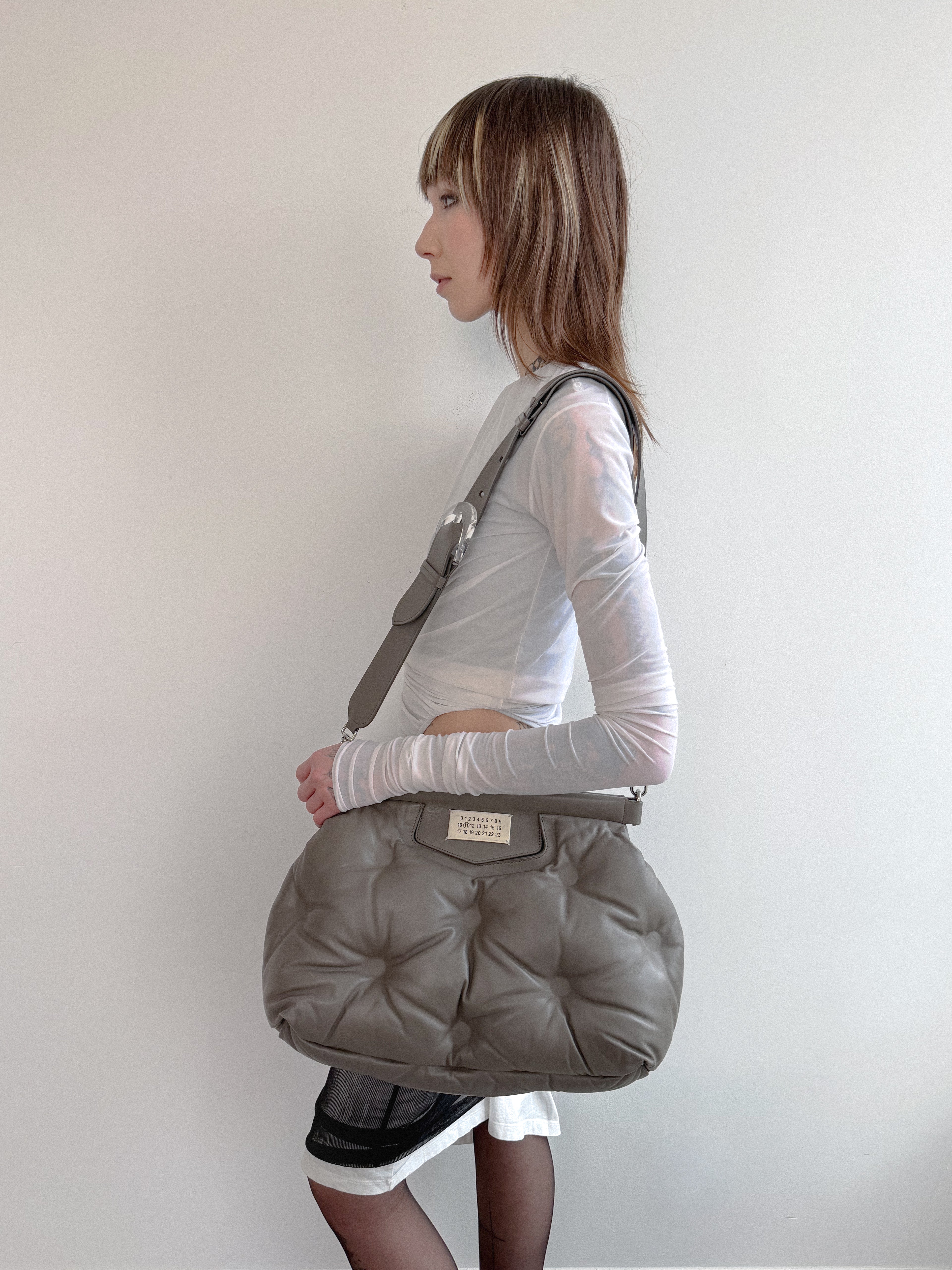Woman carrying a large gray bag on her shoulder against a plain background