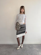 Person wearing a gray and white outfit with a patterned skirt against a plain background