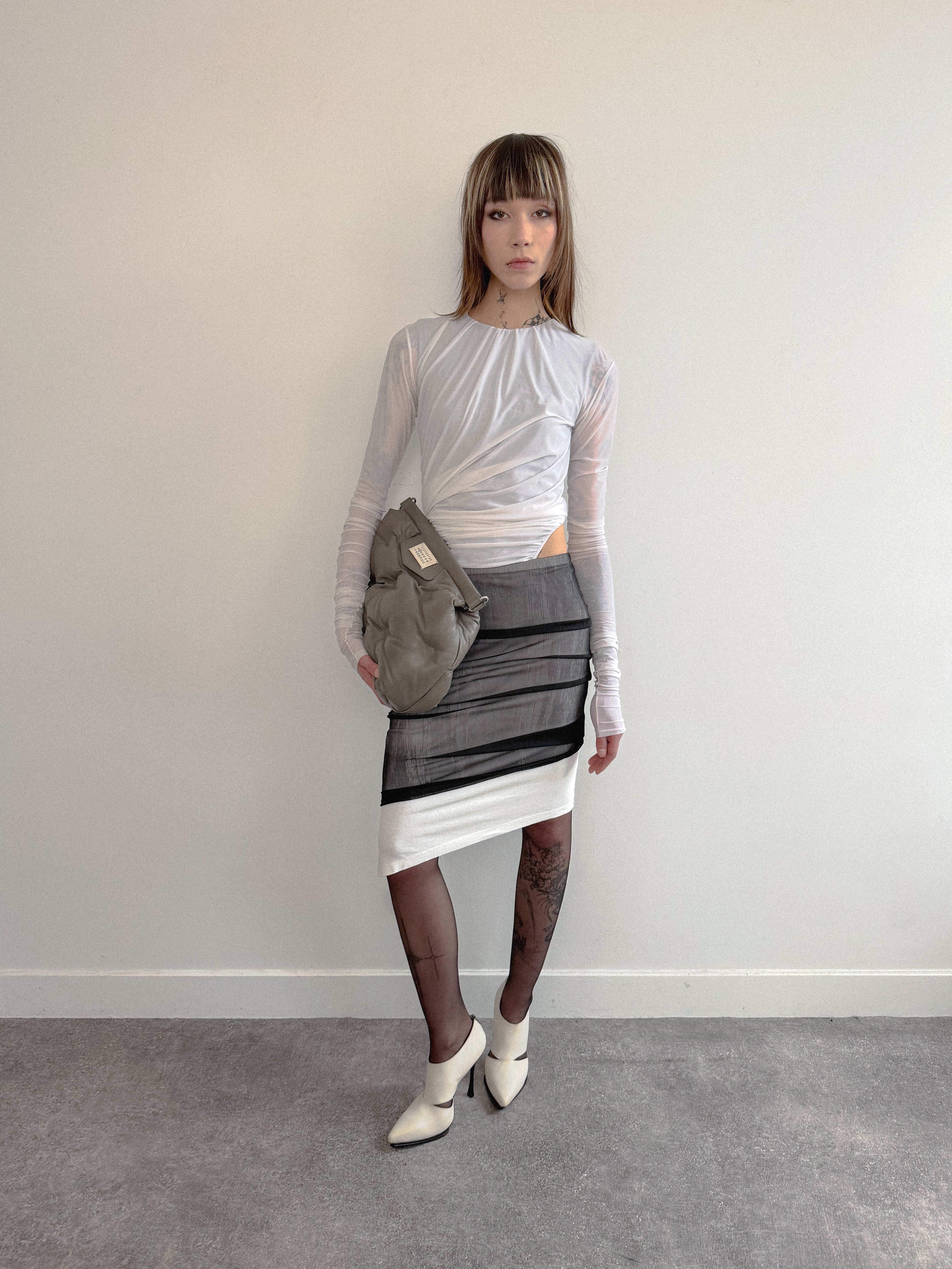 Person wearing a gray and white outfit with a patterned skirt against a plain background