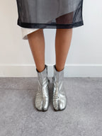 Person wearing silver tabi boots with a sheer black skirt on a neutral background