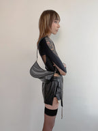 Person wearing a black outfit with a silver bag against a plain background