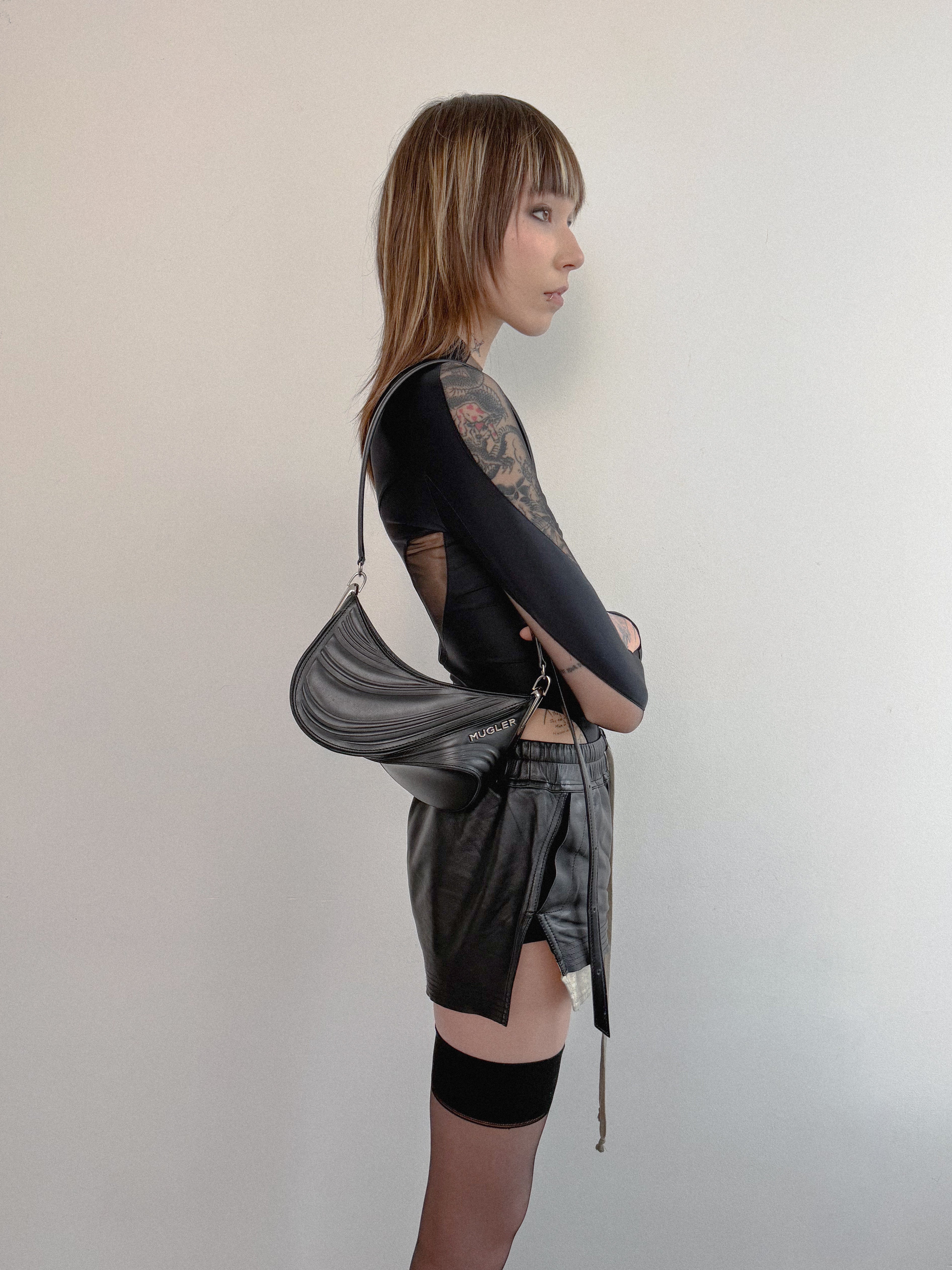 Person wearing a black outfit with a silver bag against a plain background
