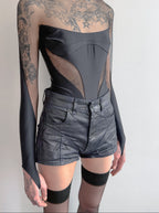 Person wearing a sheer long-sleeve top with floral patterns and black high-waisted shorts on a plain background.