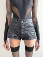 Person wearing a black bodysuit with sheer panels and high-waisted black shorts on a plain background