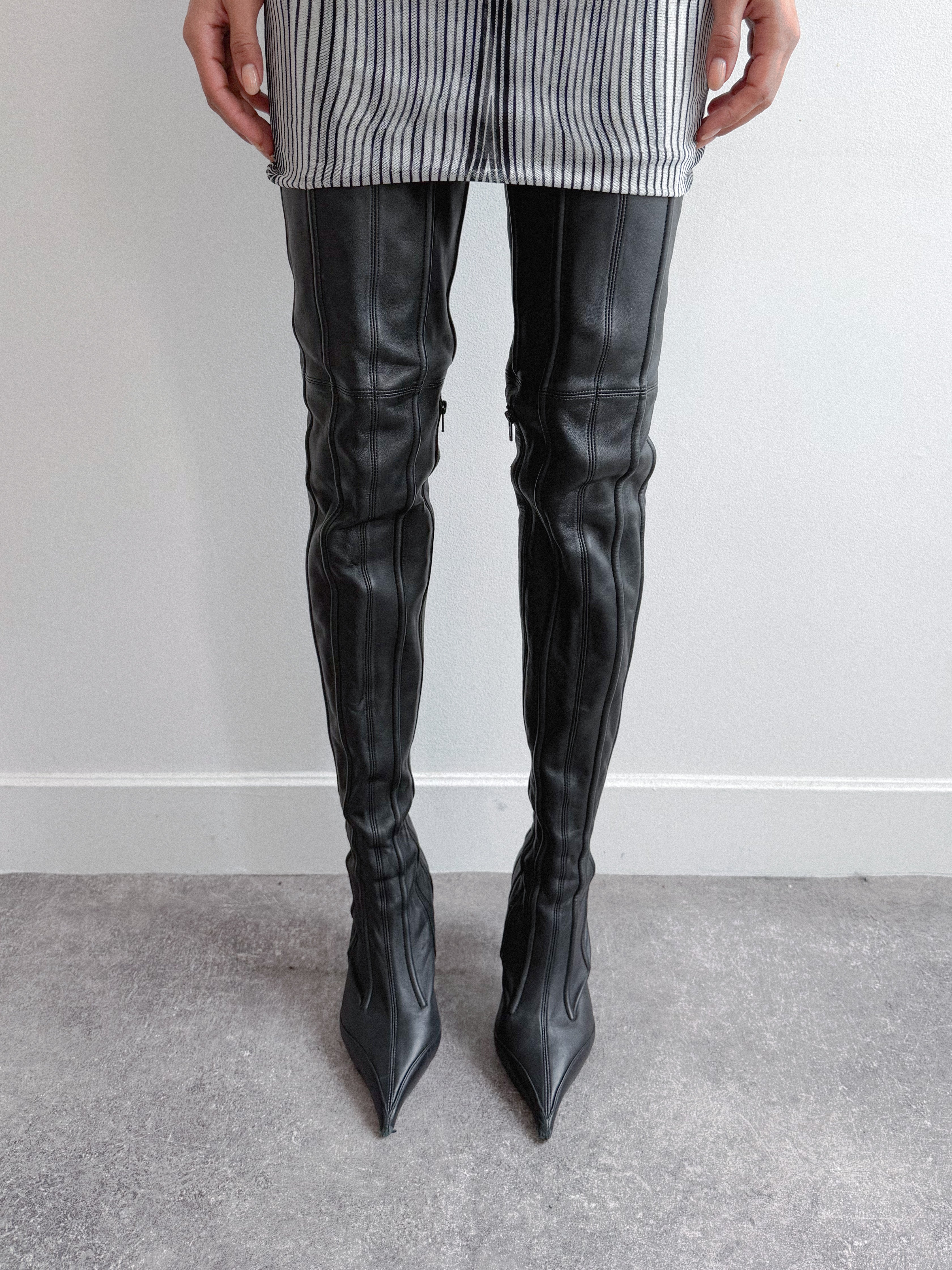 Person wearing black thigh-high boots with a plain background
