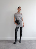 Person wearing a gray knit dress with black high-heeled boots against a white wall.