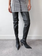 Person wearing black leather thigh-high boots with a plain background