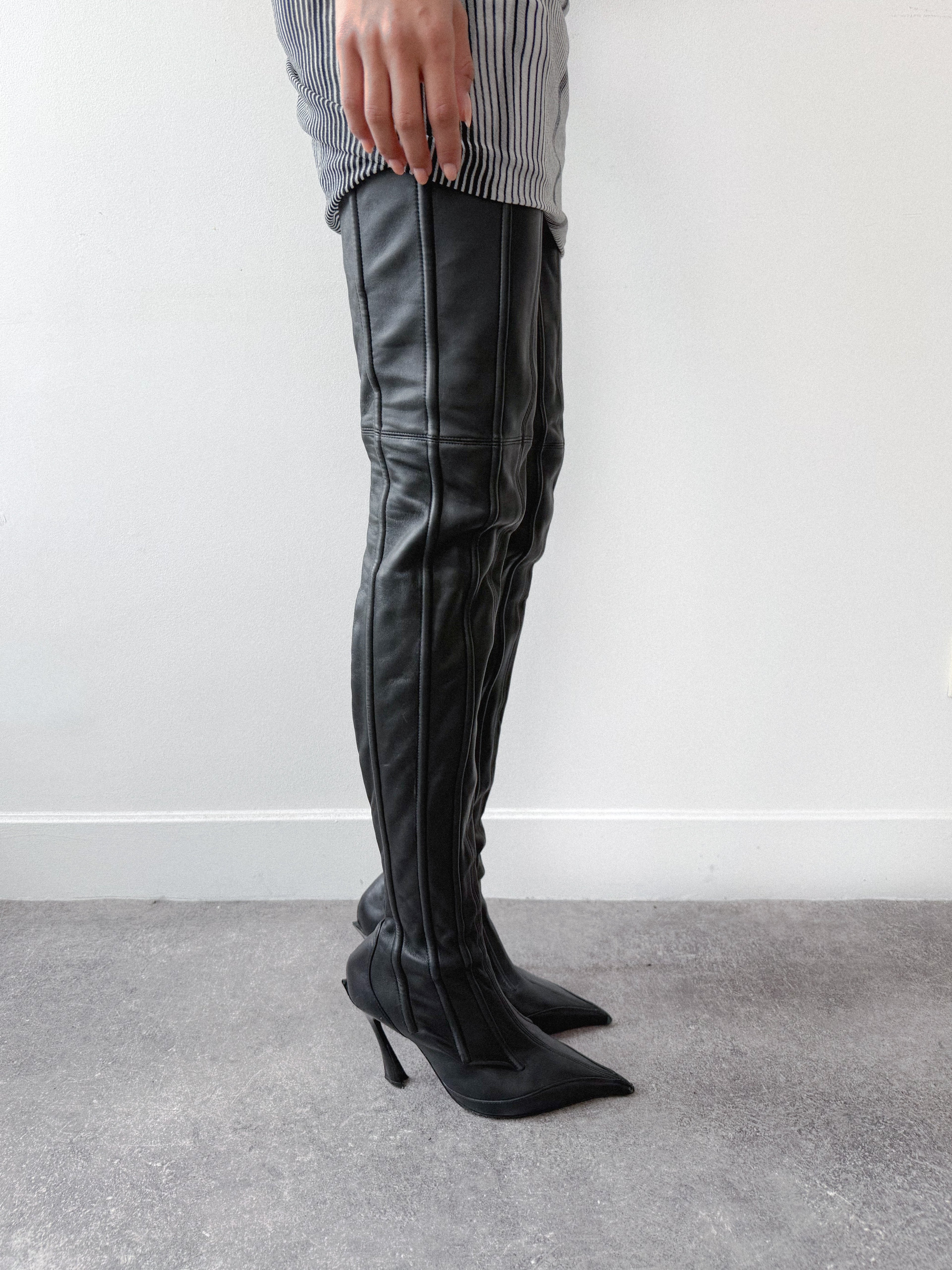 Black leather thigh-high boots worn by a person against a plain background