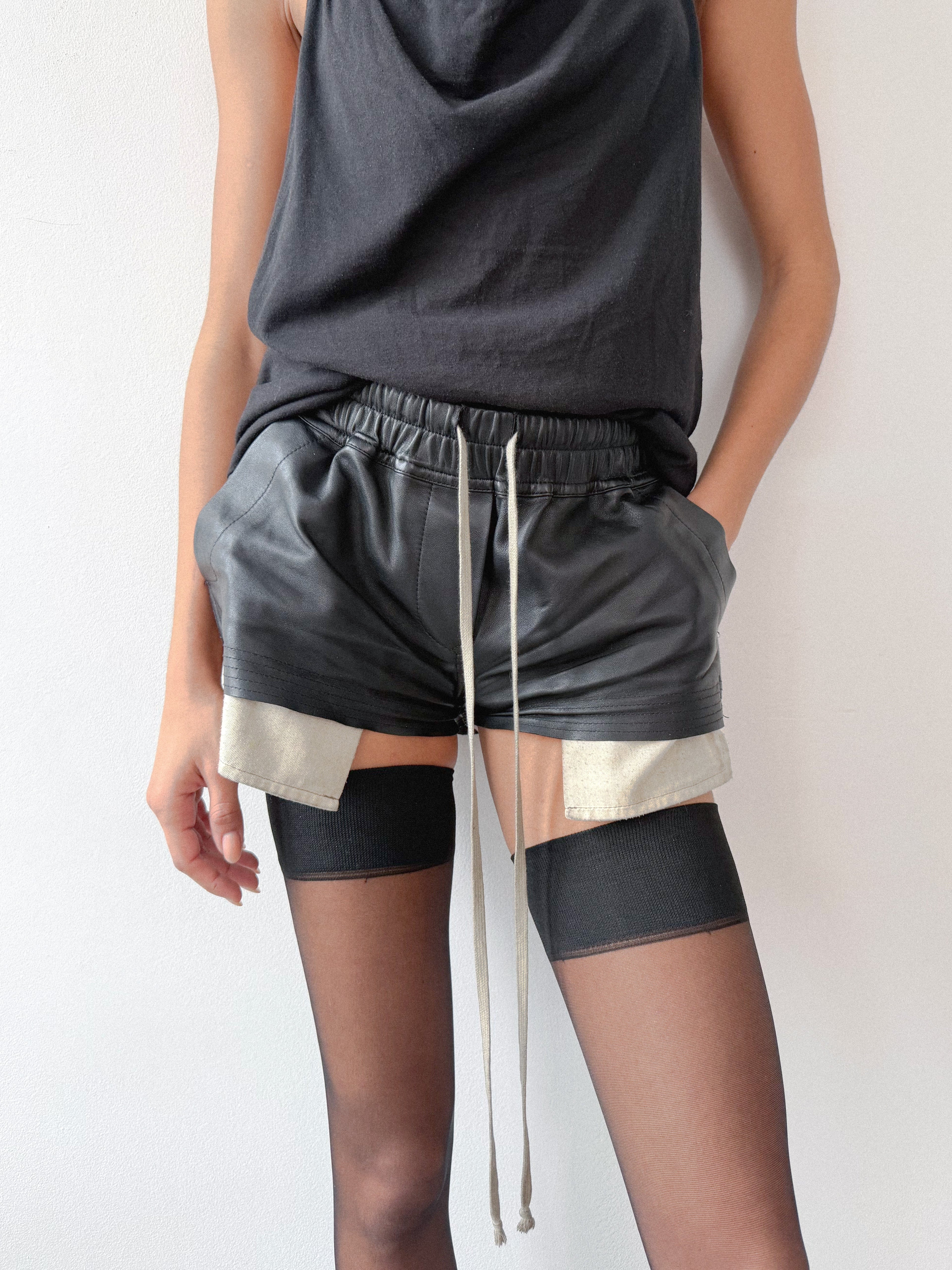 Person wearing a black sleeveless top and gray shorts with a white drawstring on a plain background