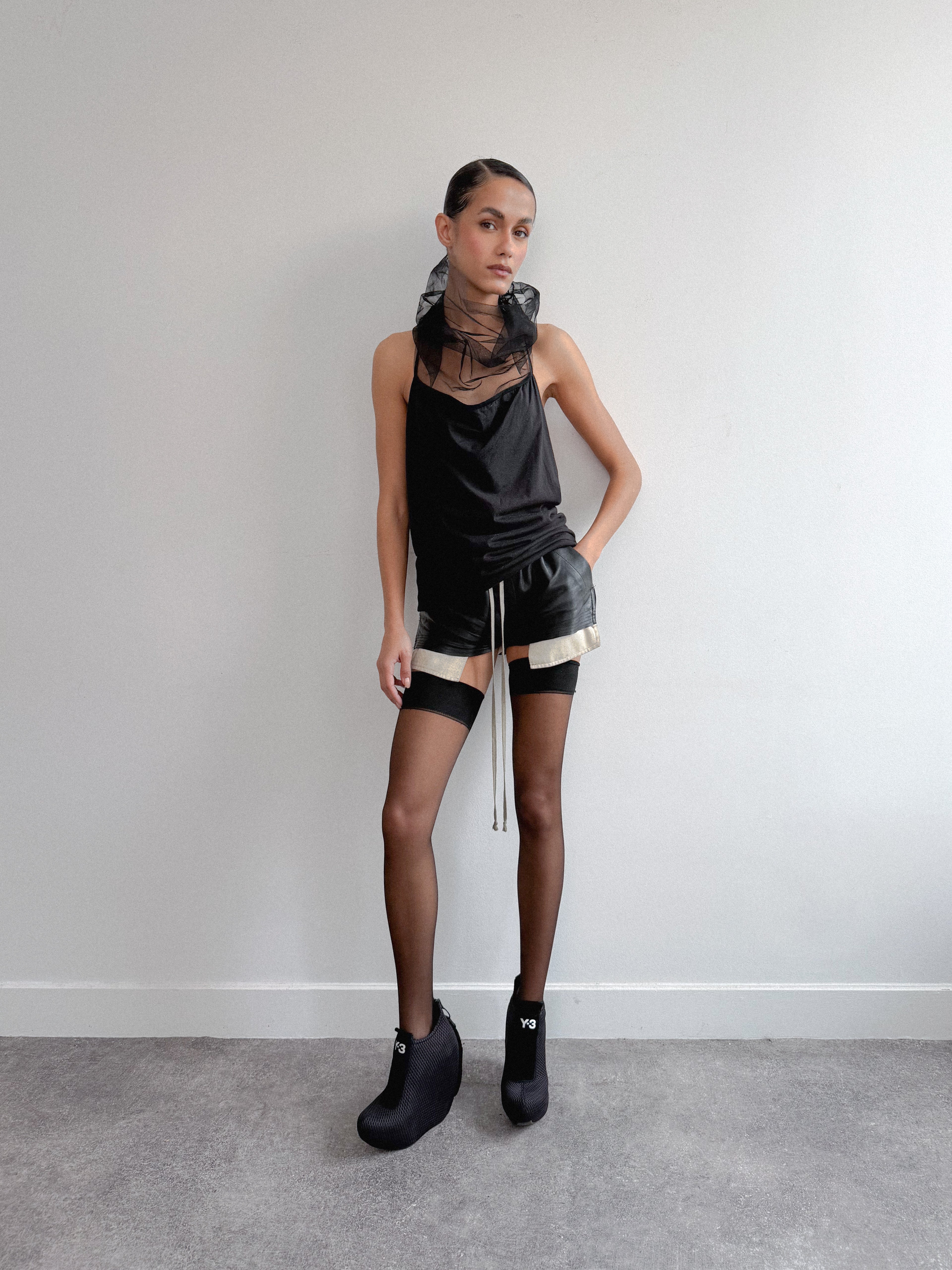 Person wearing a black outfit with sheer elements against a plain background