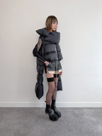Person wearing a futuristic, layered outfit with a large hood against a plain background