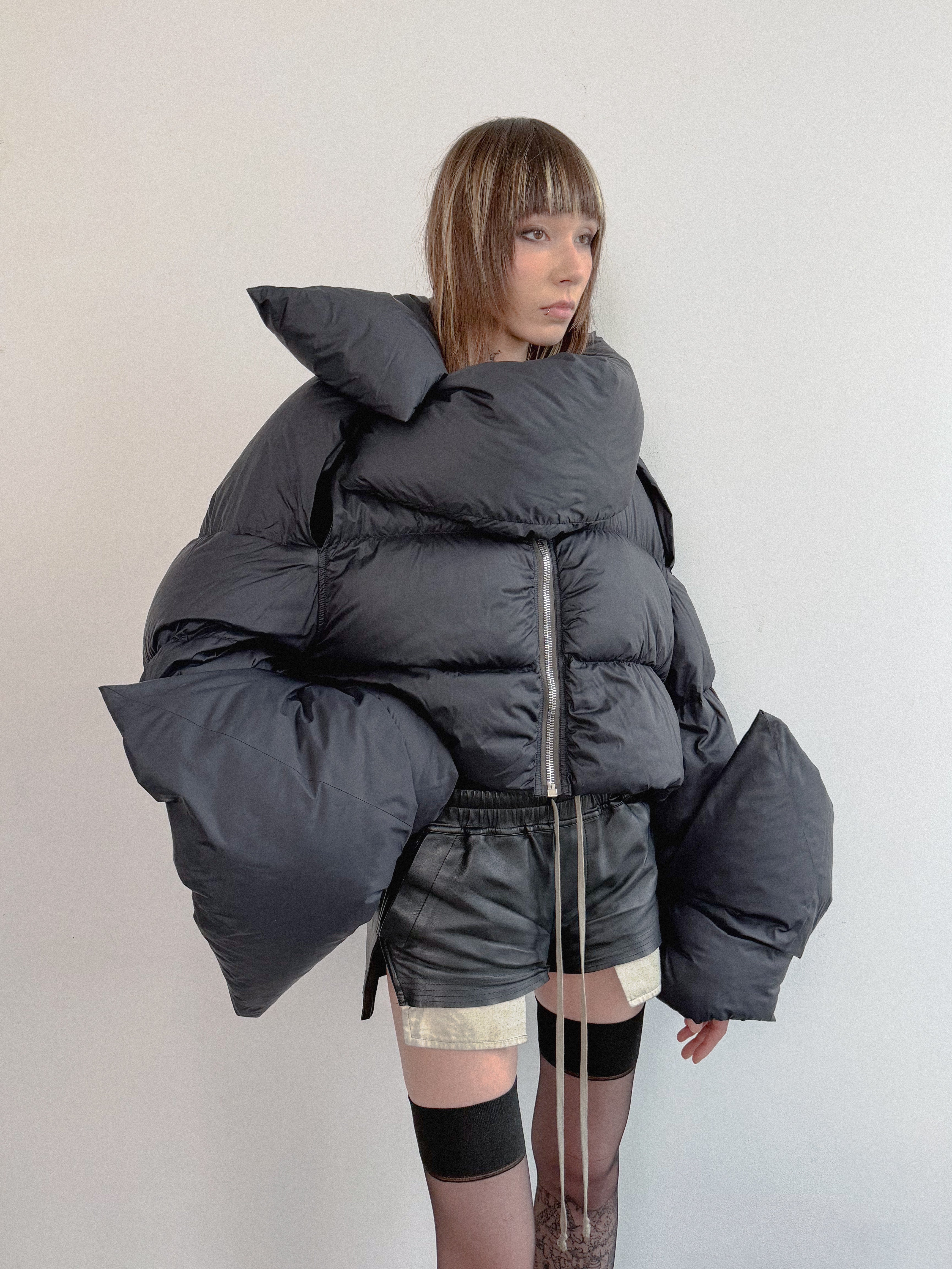 Person wearing a large dark gray puffer jacket against a plain background