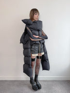 Person wearing a unique, layered black outfit with a puffer jacket against a plain background