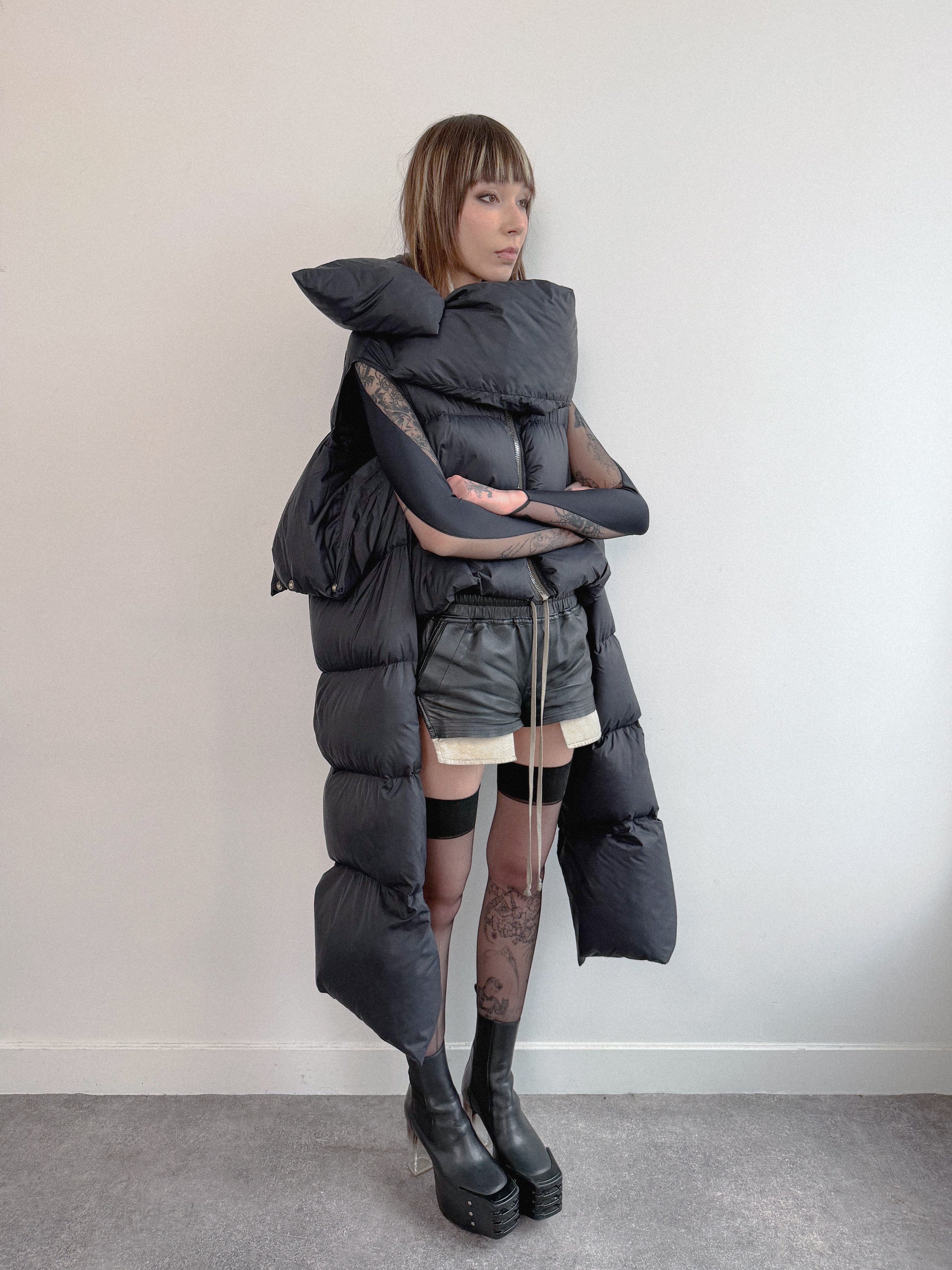 Person wearing a unique, layered black outfit with a puffer jacket against a plain background