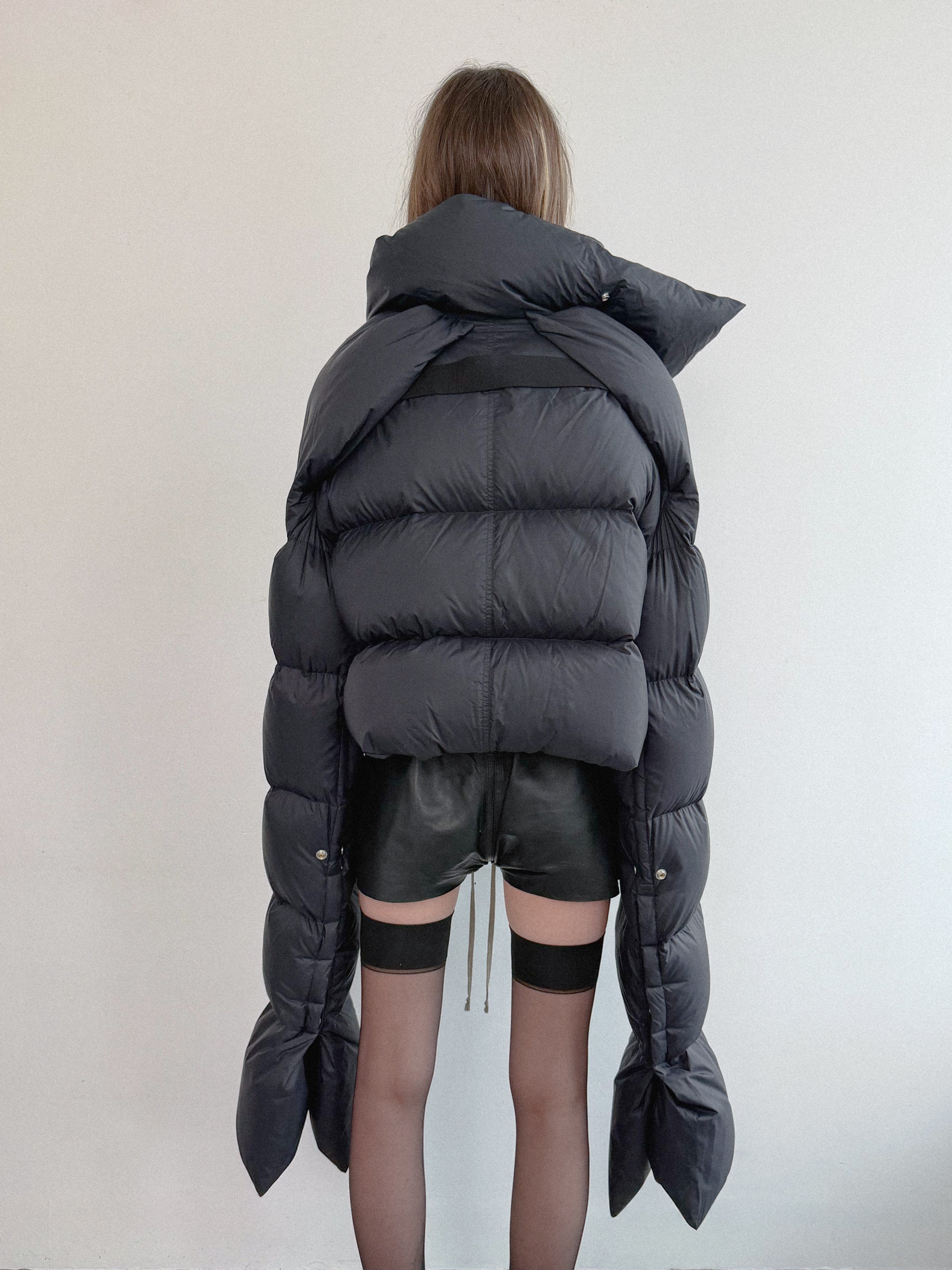 Person wearing a large black puffer jacket with a plain background