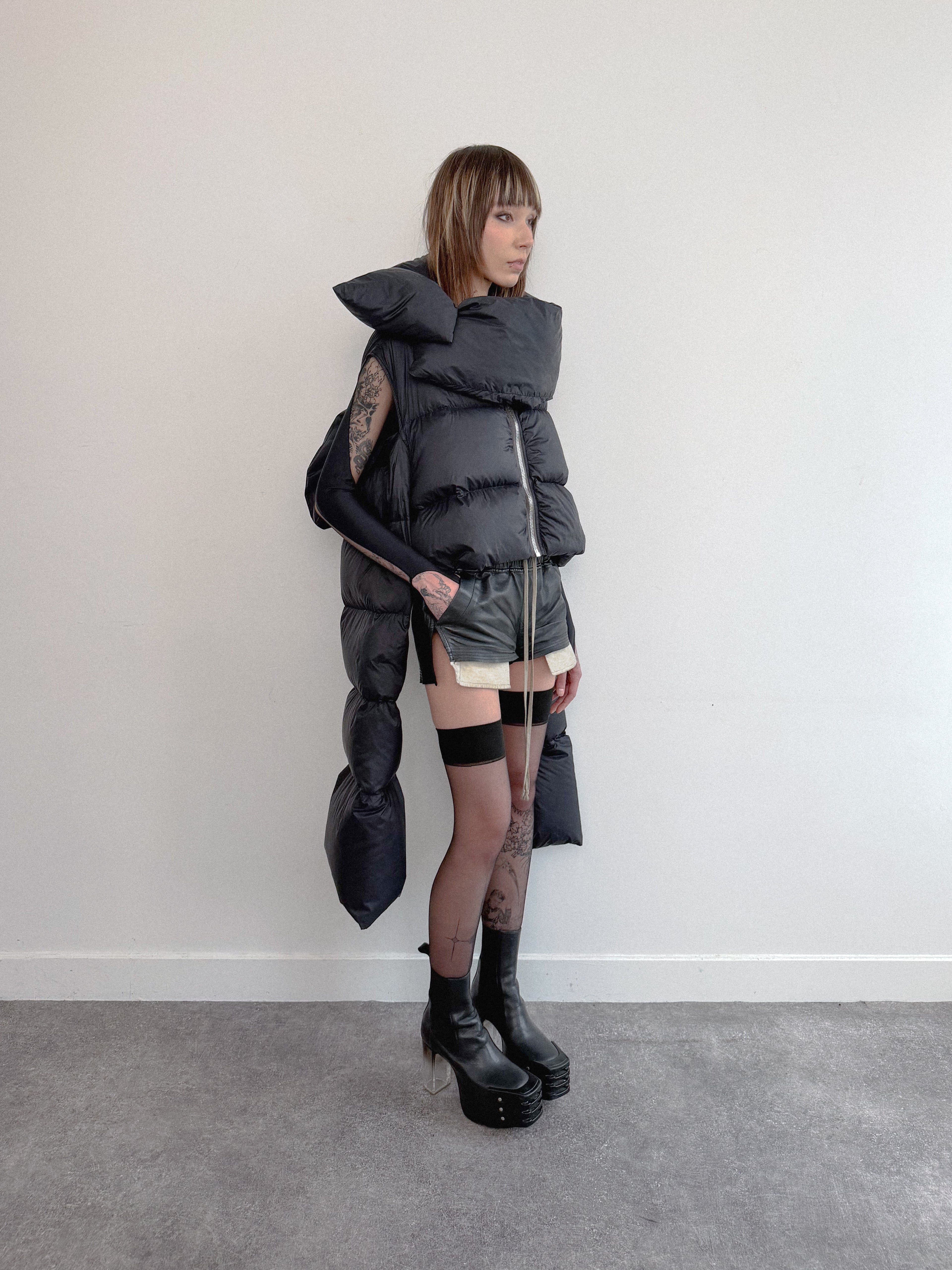 Person wearing a futuristic, layered outfit with a large hood against a plain background
