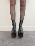 Black platform boots worn with sheer black tights against a plain background