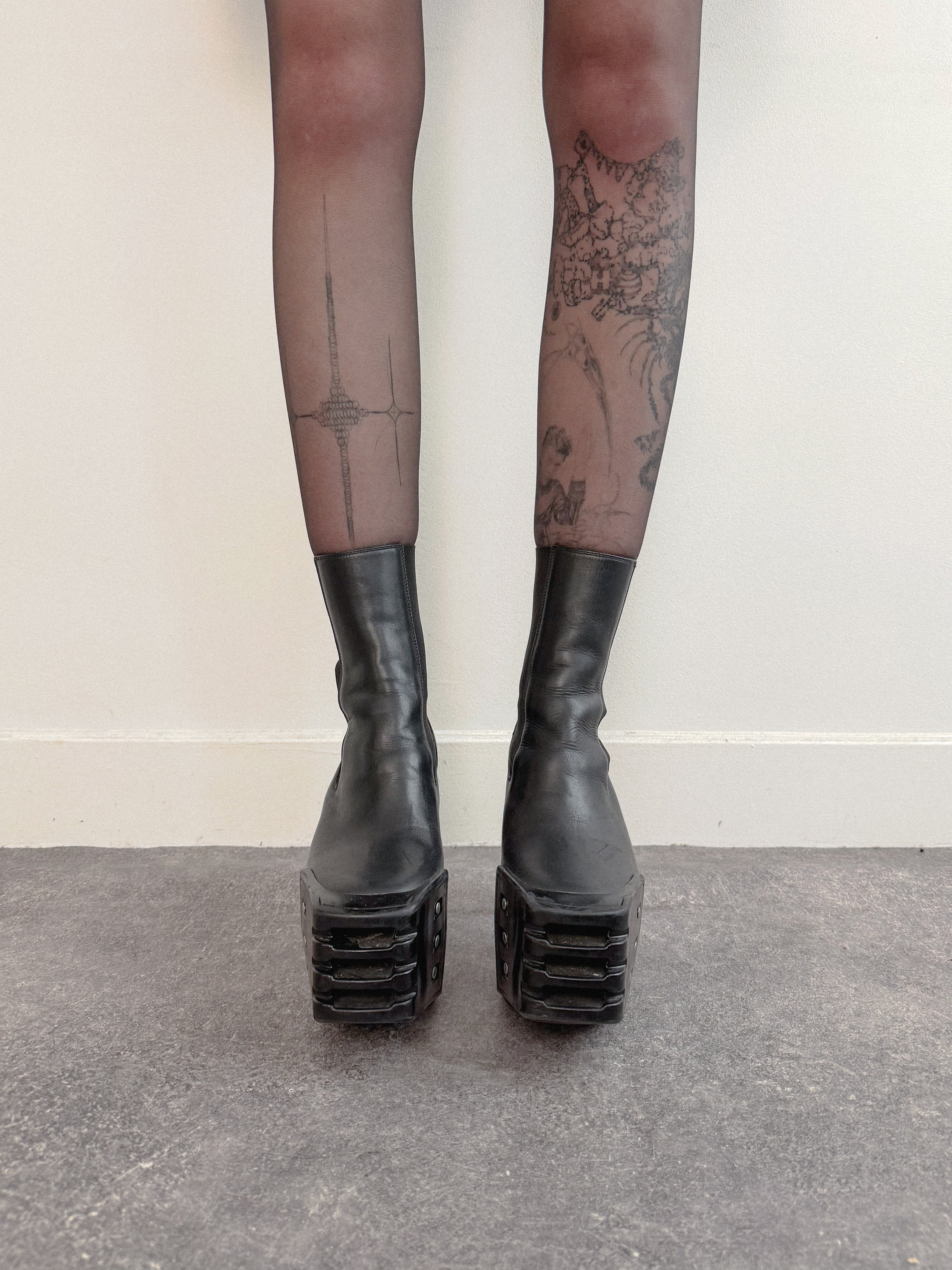Black platform boots worn with sheer black tights against a plain background