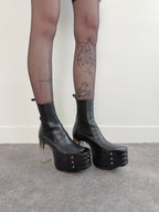 Black platform boots worn with sheer black tights against a plain background