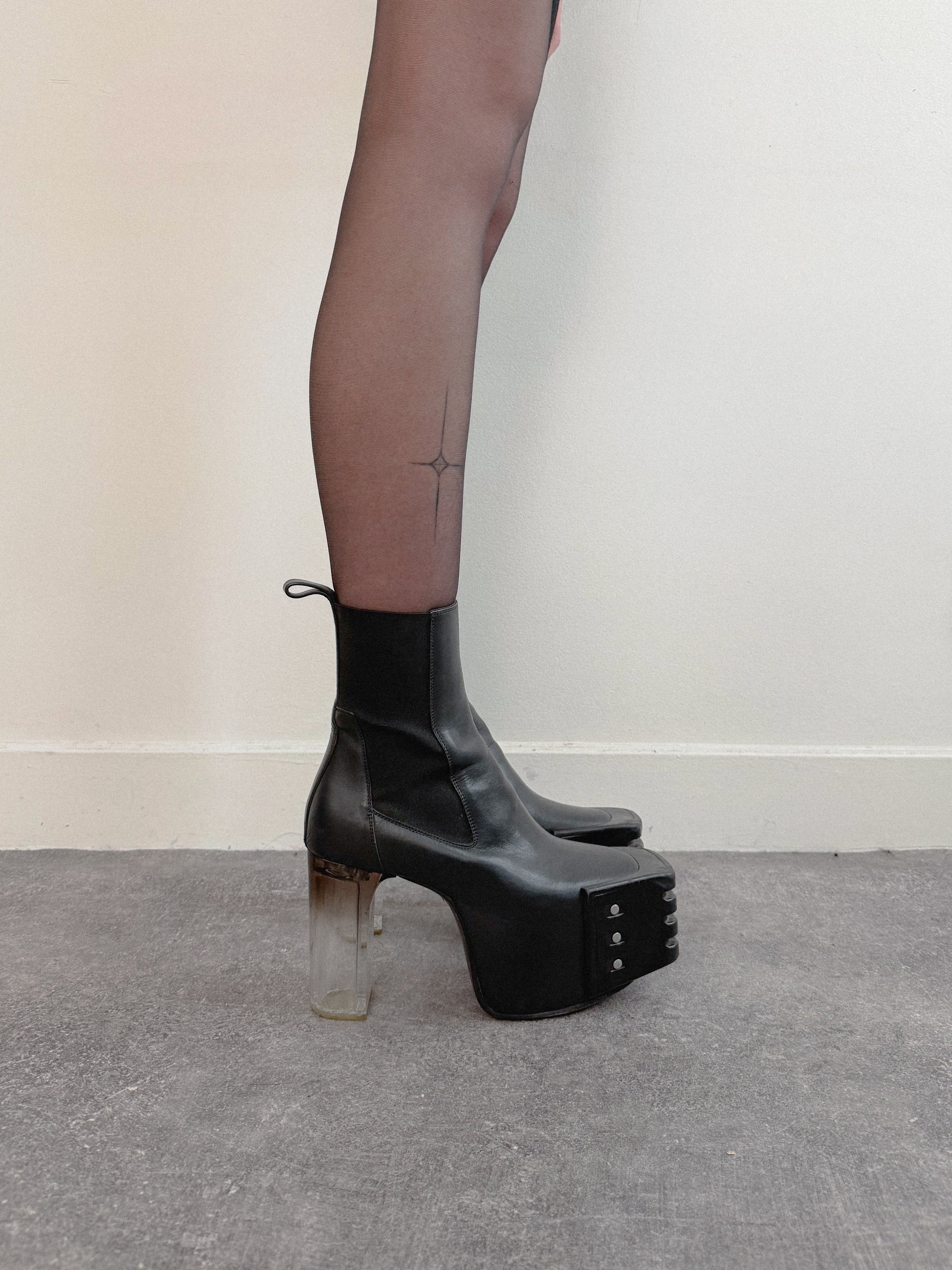 Black platform boots worn with sheer black tights on a neutral background