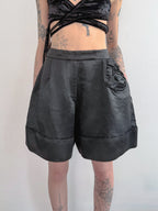 Person wearing black leather shorts on a plain background