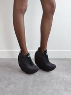 Black textured ankle boots worn with tights on a neutral background